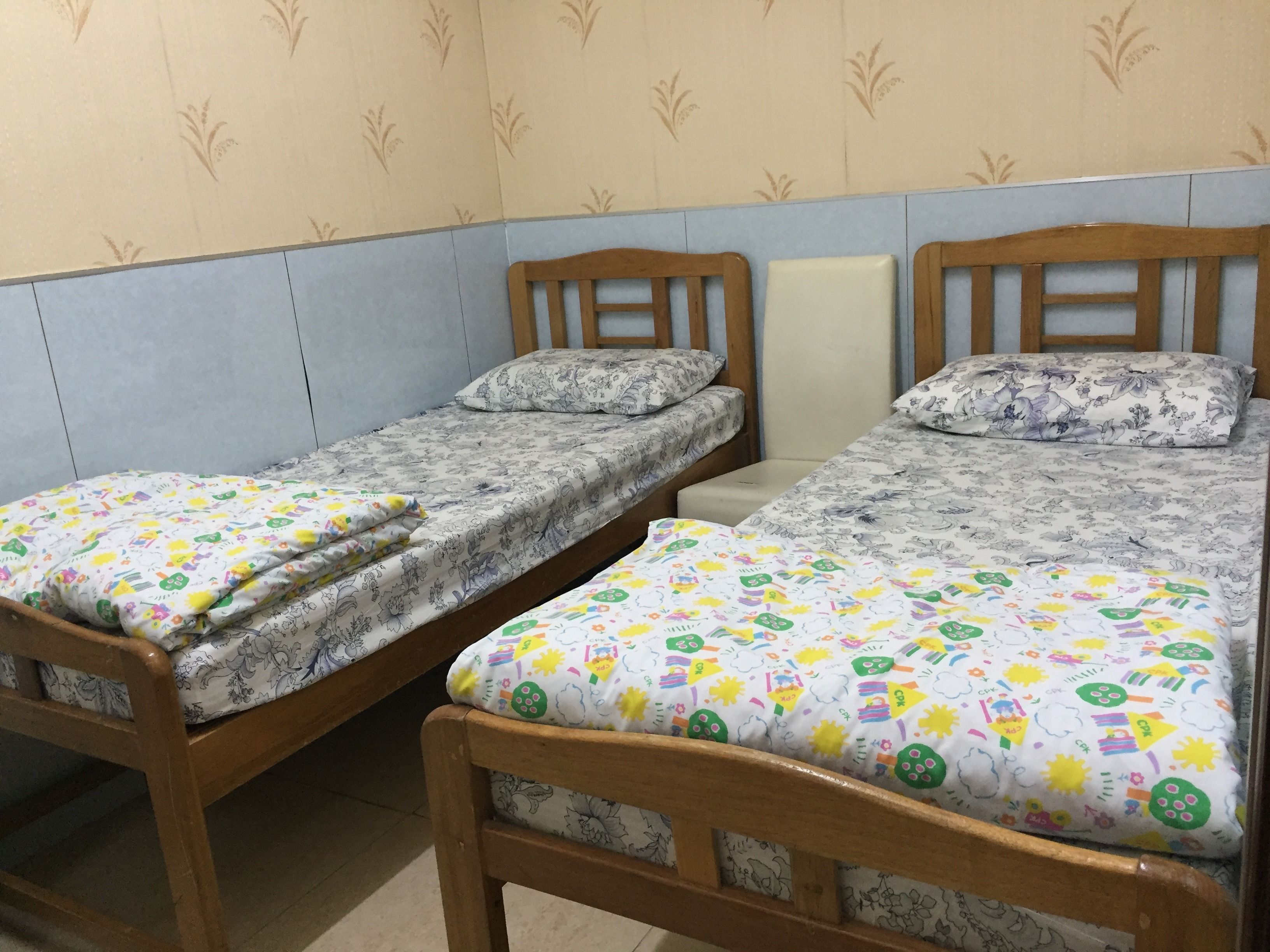 Two wooden beds with floral bedding, a tiled wall, and a patterned wallpaper.