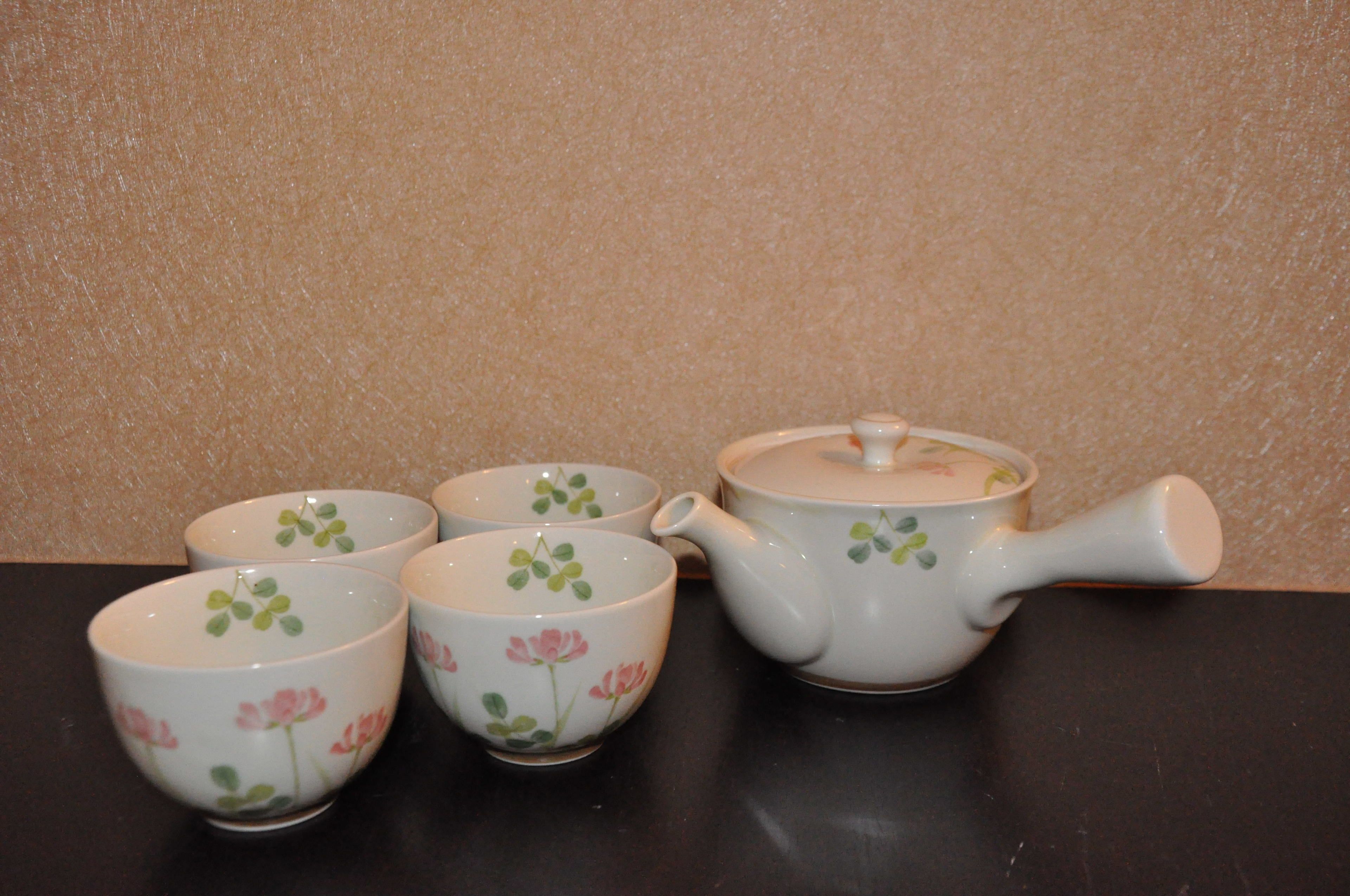 A set of white teacups and a teapot with floral designs on a dark surface.