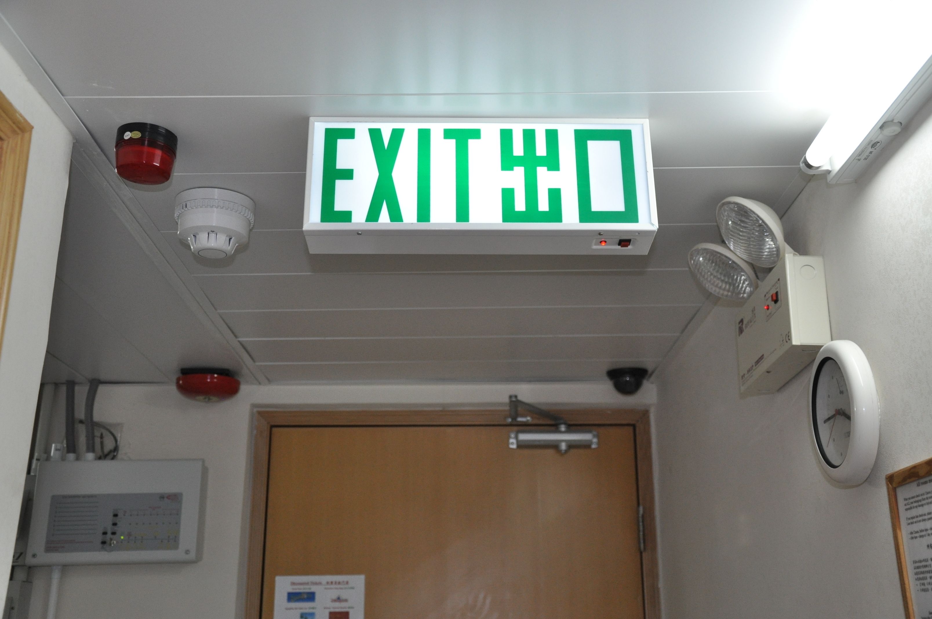 An exit sign, a fire alarm, and a clock on the wall.