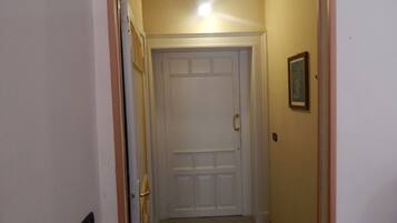 A narrow hallway with a white door at the end, a framed picture on the wall, and a light fixture above the door.