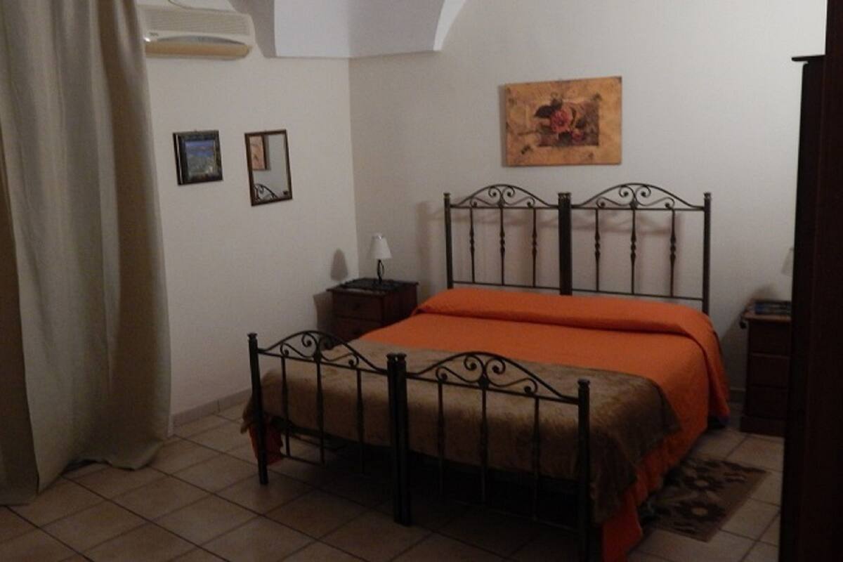 Un dormitorio con cama, mesita de noche, lámpara y un cuadro en la pared.