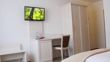 A hotel room with a bed, a desk with a chair, a television mounted on the wall, and a wardrobe.