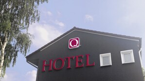 Une enseigne d’hôtel avec le mot « HÔTEL » écrit en lettres rouges et un logo au-dessus.