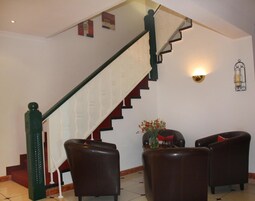 Una escalera con barandilla blanca y peldaños negros, que conduce a un rellano con dos sillones de cuero y una mesita con un florero.