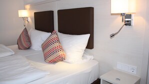 Une chambre d’hôtel avec un lit bien fait, deux lampes fixées au mur et une table de chevet avec une télécommande.