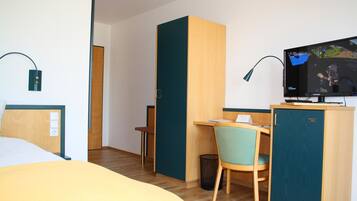 Een hotelkamer met een bed, bureau, stoel, televisie en een prullenbak.