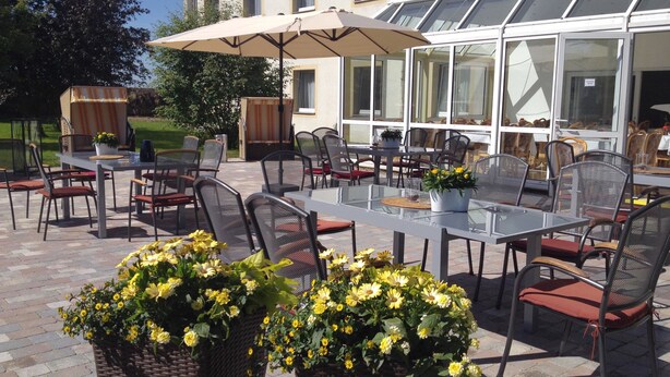 Une terrasse extérieure avec des tables et des chaises, un grand parasol et des plantes en pot.