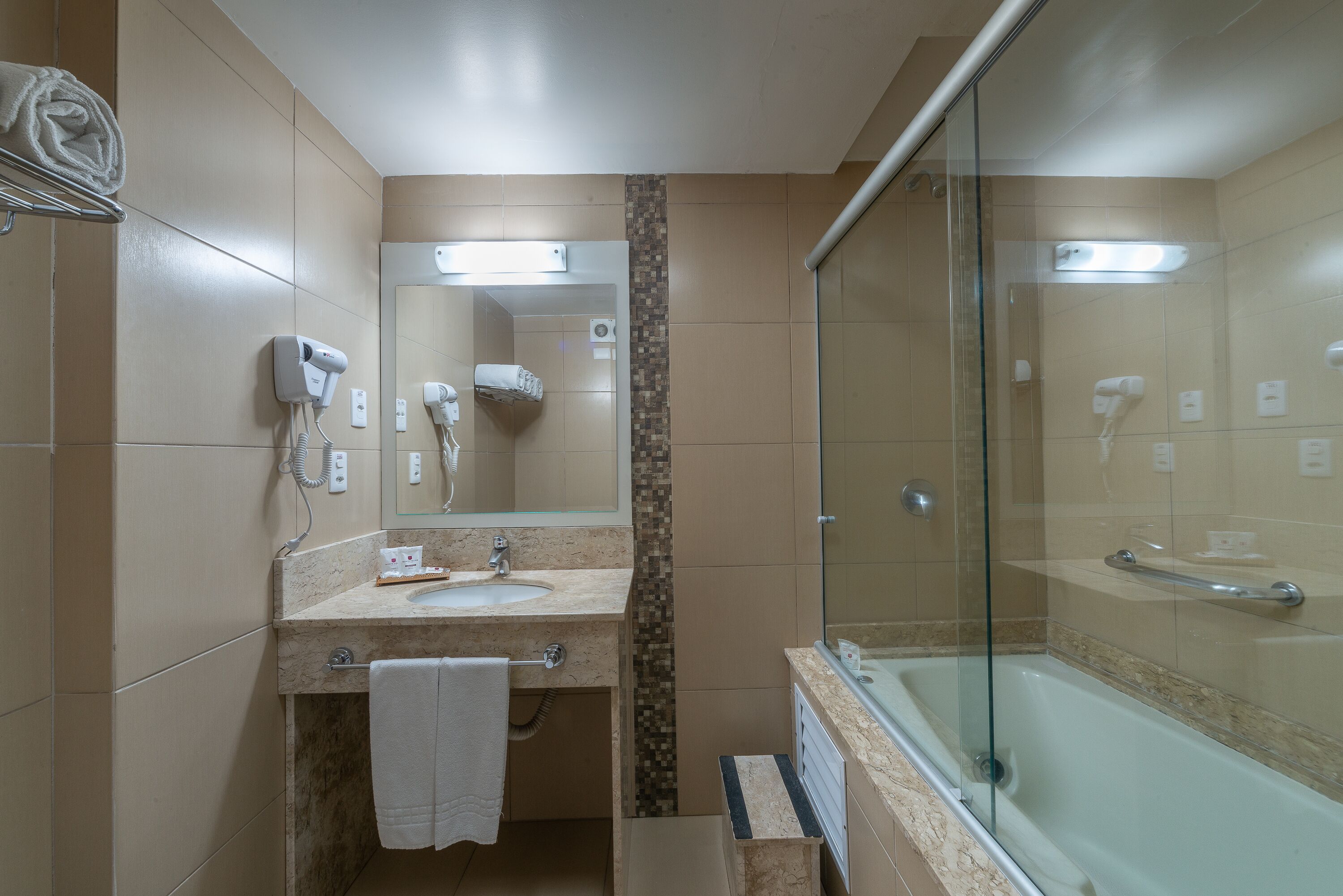Un baño con ducha separada por mampara de vidrio, un lavamanos y un perchero para toallas.