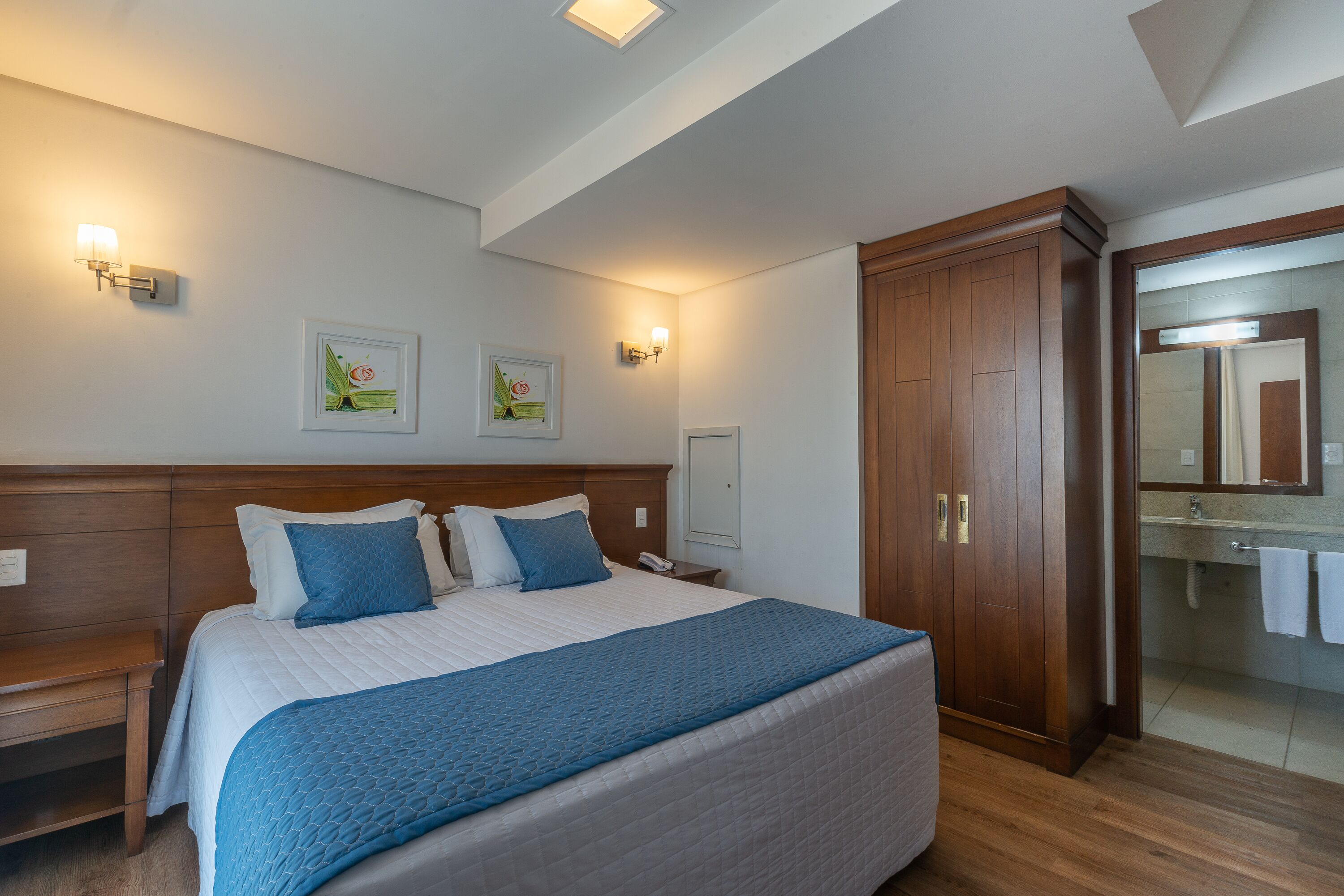 Habitación de hotel ordenada con una cama grande, mesitas de noche, un armario y un baño con espejo y lavabo.