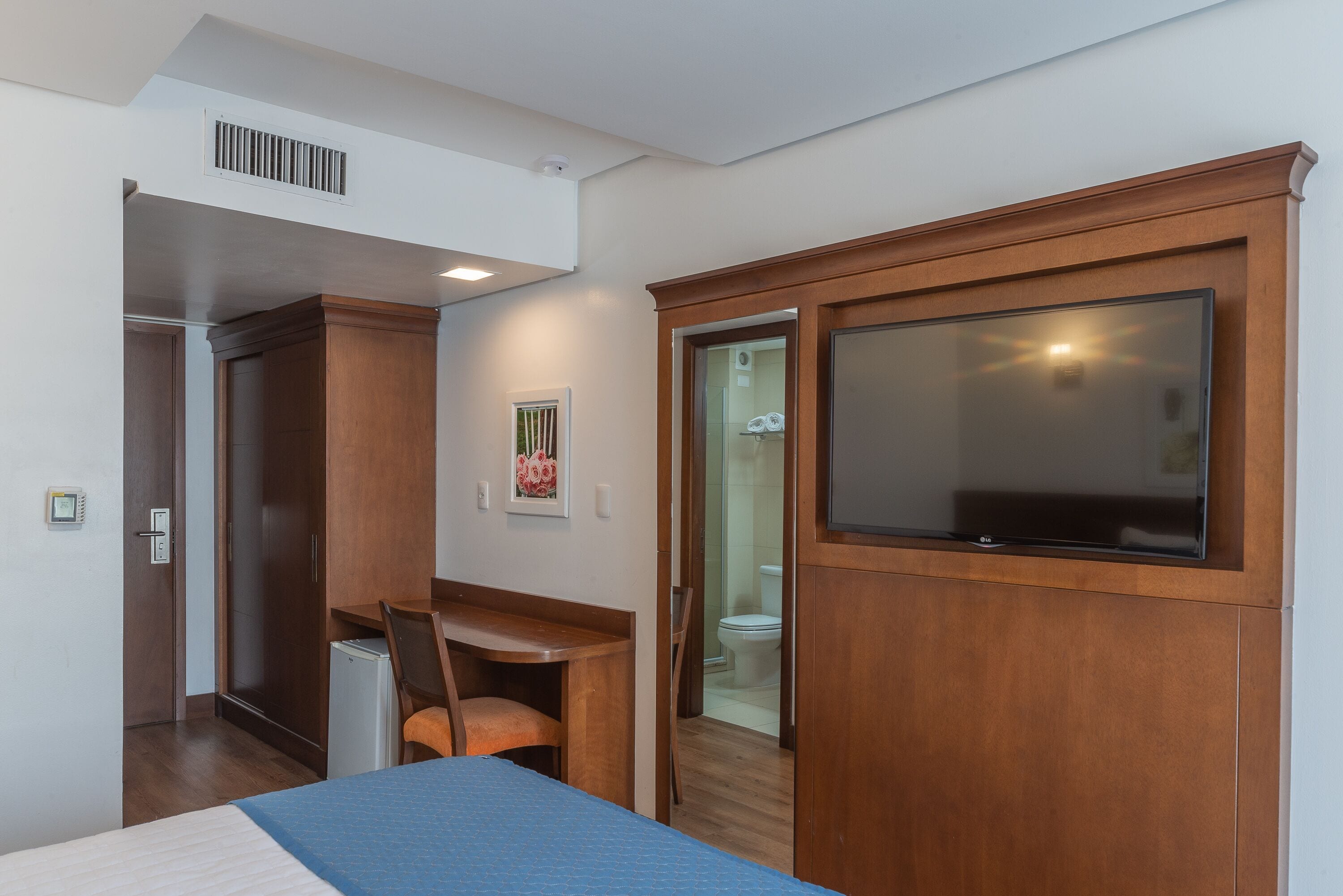 Una habitació d'hotel amb un llit, una taula de nit, una cadira, un televisor i un armari.