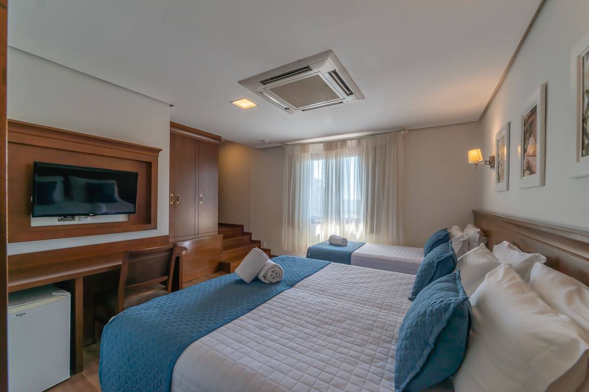 Una habitación de hotel con una cama, un escritorio, un televisor y una ventana con cortinas.