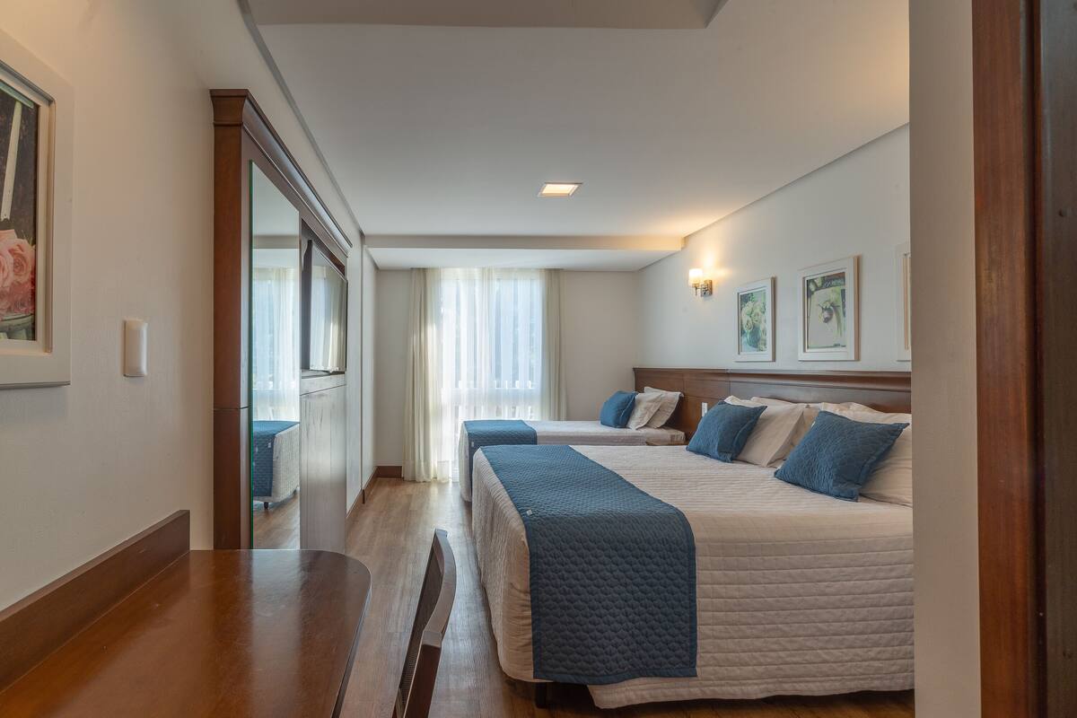 Una habitación de hotel con dos camas, un banco de madera, un espejo grande y obras de arte en la pared.