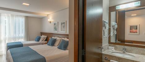 Ein Hotelzimmer mit zwei Betten, einem Badezimmer mit Waschbecken und Spiegel sowie einem Fenster mit Vorhängen.