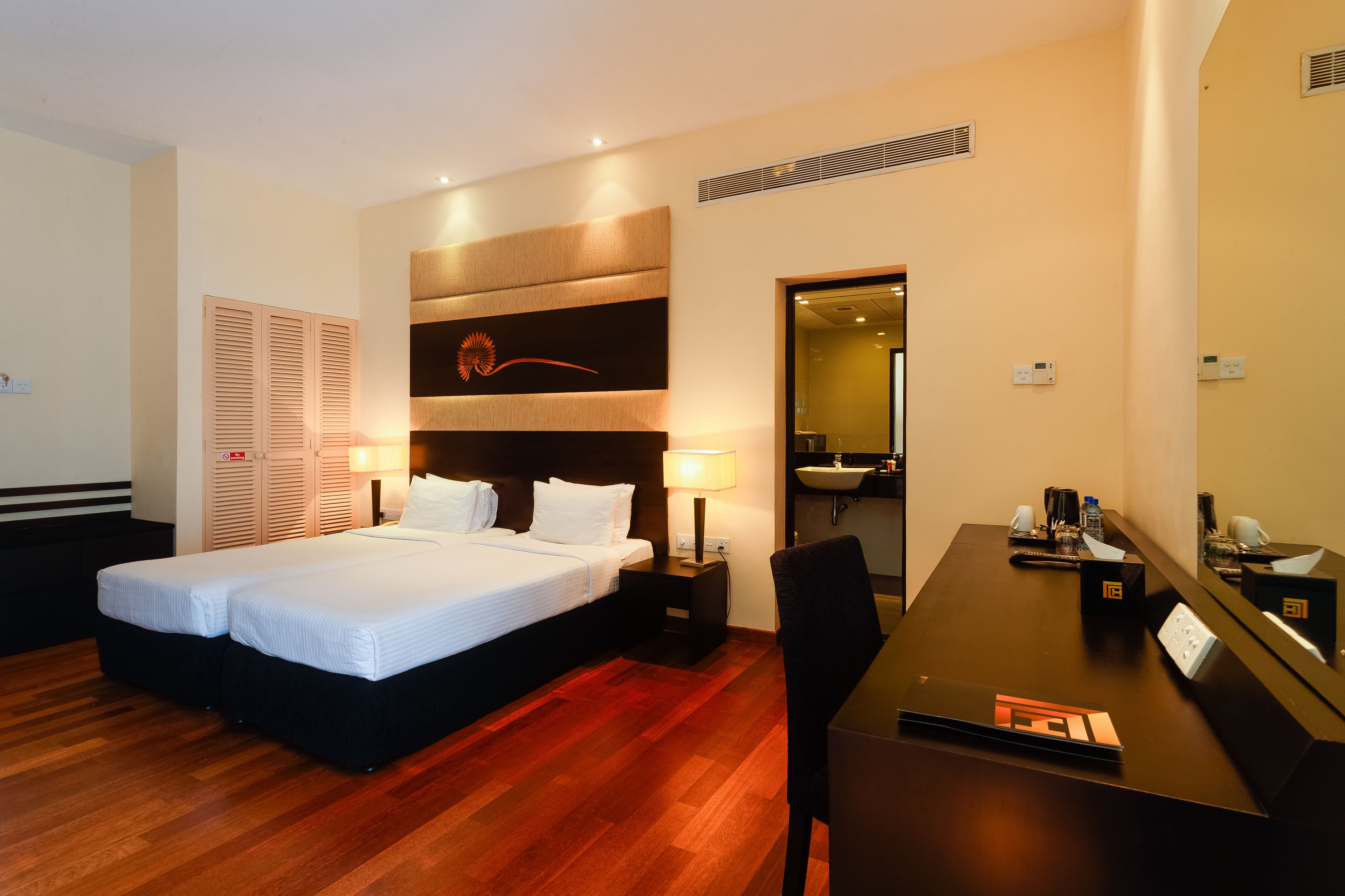A hotel room with a double bed, a desk with a chair, a mirror, a nightstand, and a bathroom visible through an open door.
