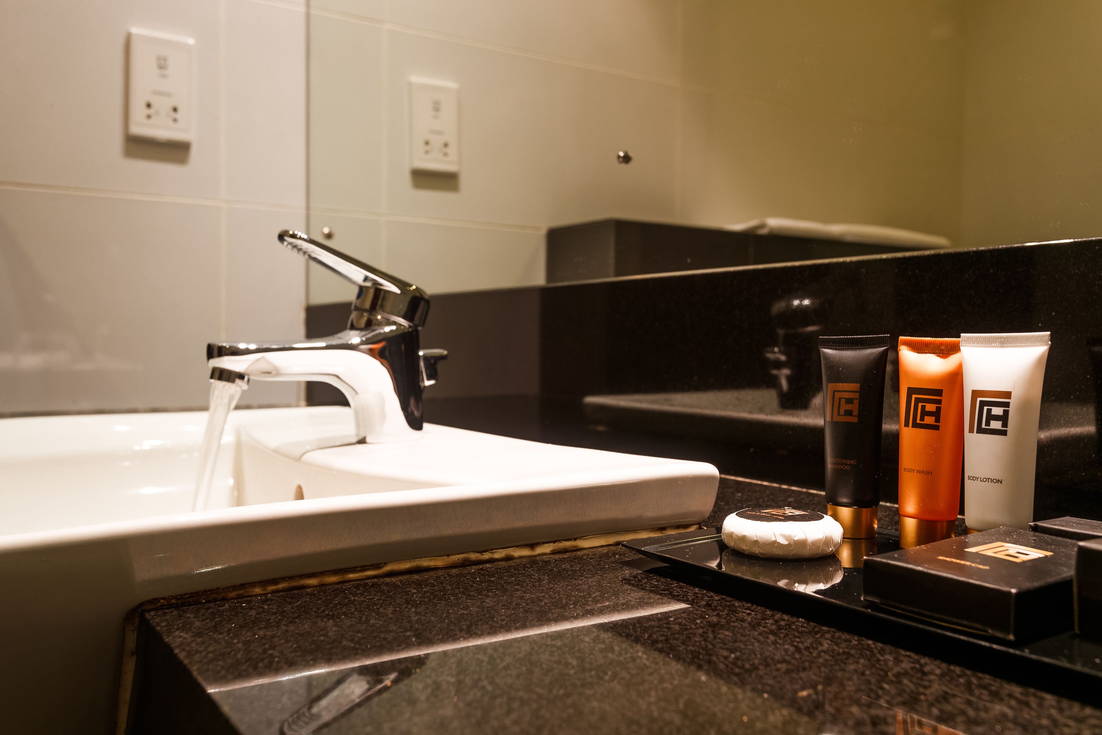 A bathroom with a sink, running water, and toiletries on the counter.