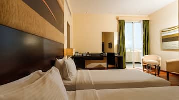 A hotel room with two beds, a desk, a chair, and a view of the outdoors.
