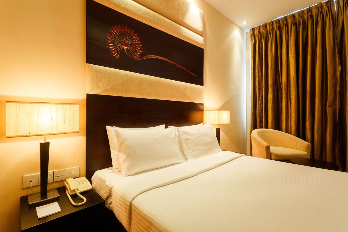 A hotel room with a large bed, two bedside lamps, a telephone, and a decorative wall piece.