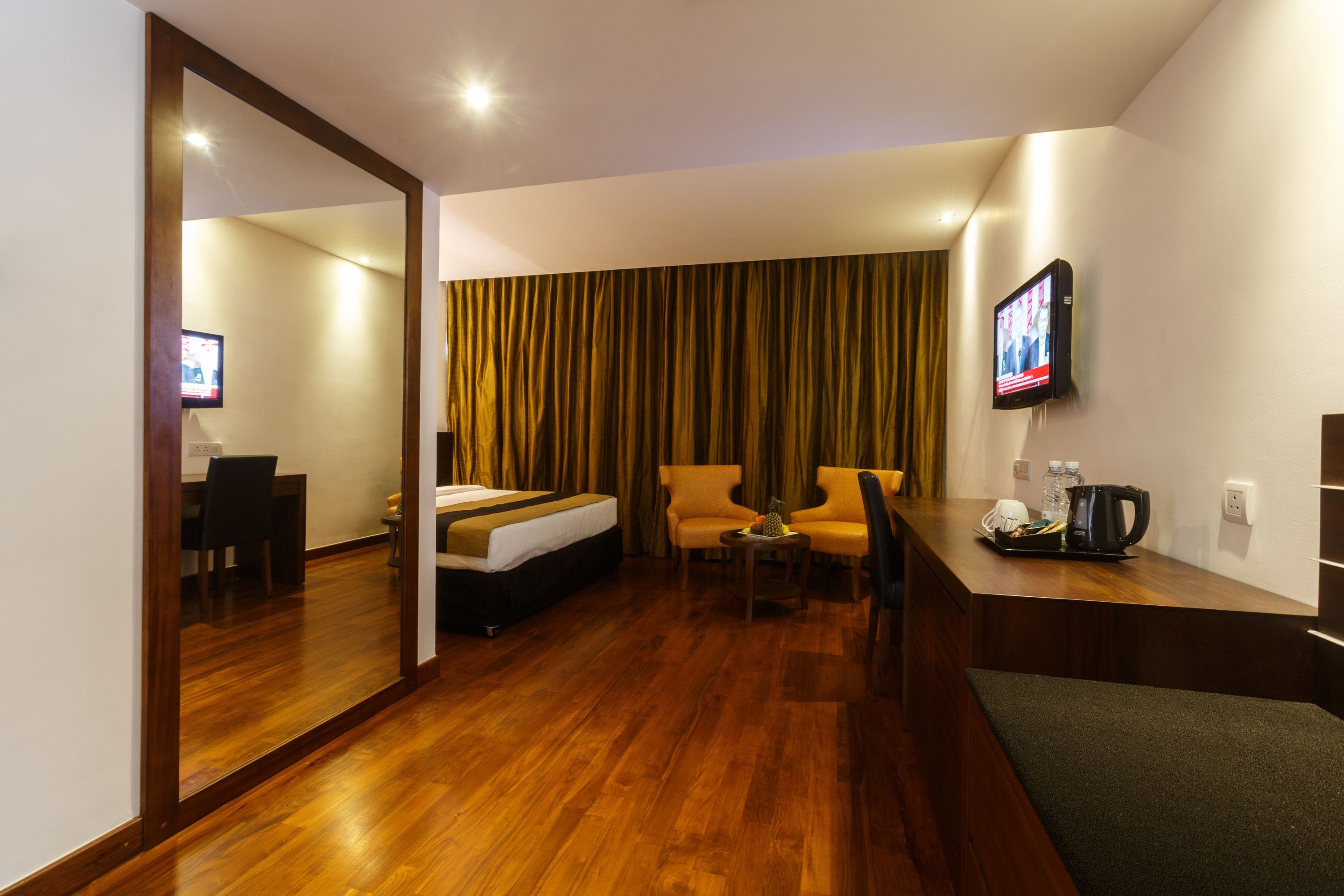 A hotel room with a wooden floor, a bed, a desk with a chair, a television, and a curtain.