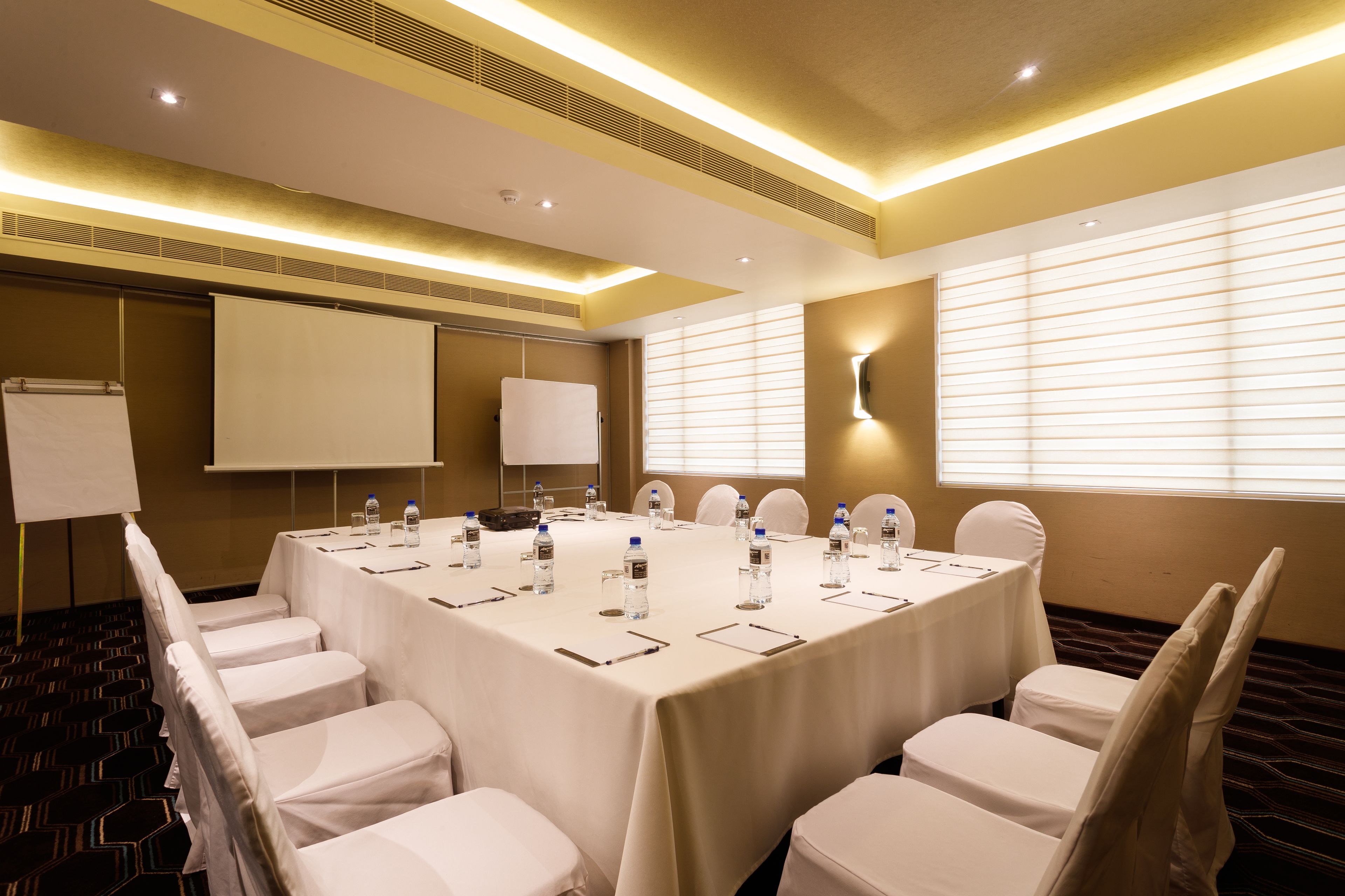 Un salón de conferencias con una gran mesa, sillas blancas y una pantalla para proyector.