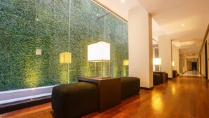 Um lobby moderno com parede verde, piso de madeira e balcão de recepção com dois sofás pretos.
