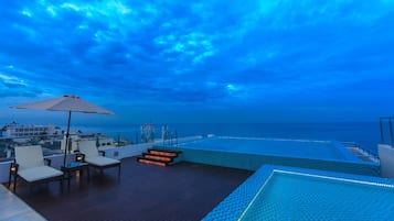Zona de piscina en la azotea con vistas al océano, sillones de descanso y una sombrilla grande.