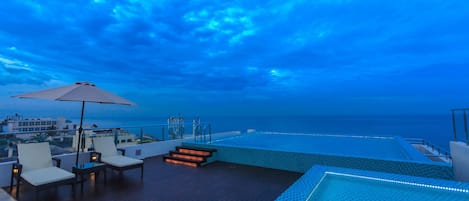 A rooftop pool area with a view of the ocean, lounge chairs, and a large umbrella.