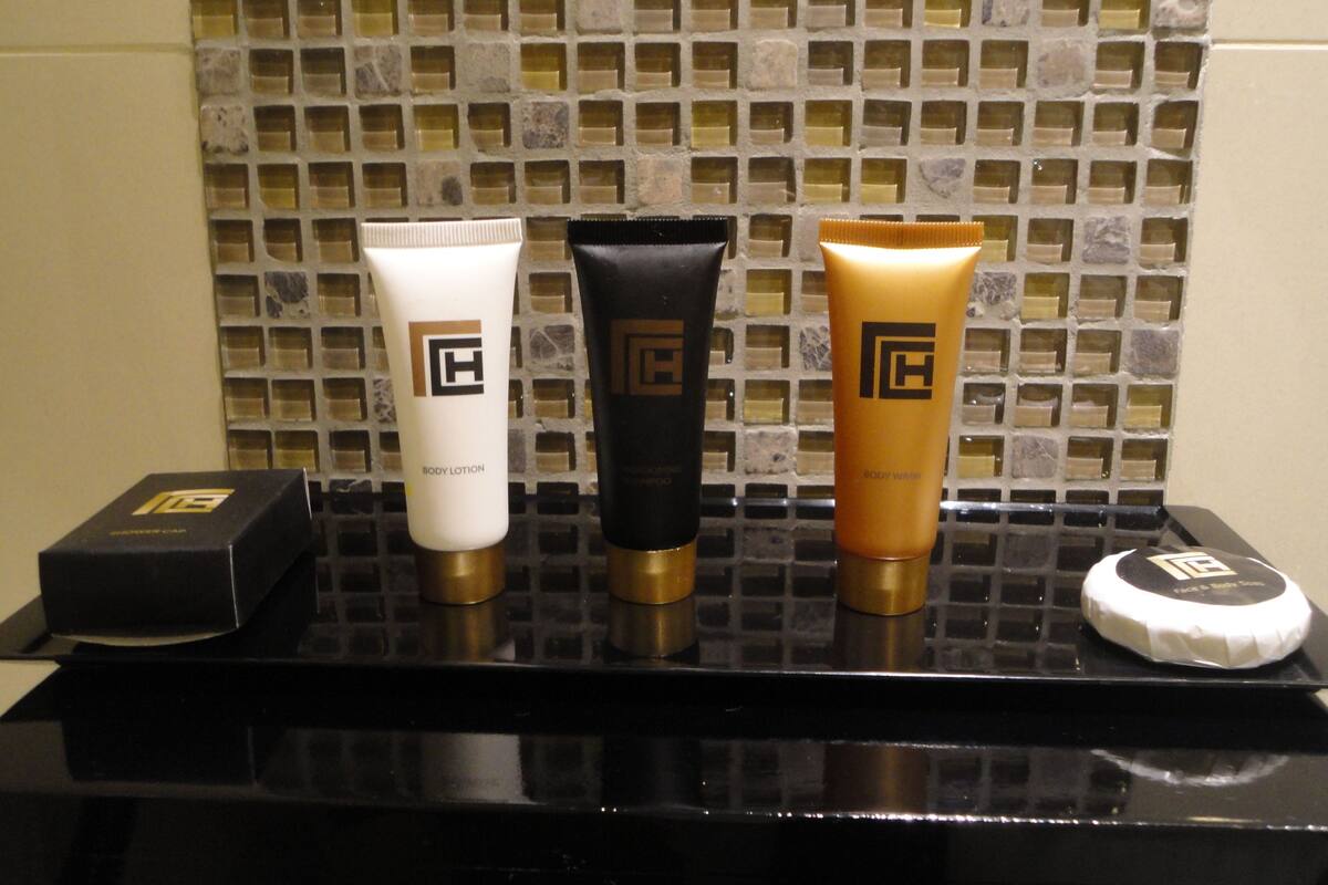 Three body lotion tubes on a black tray with a mosaic tile backsplash.