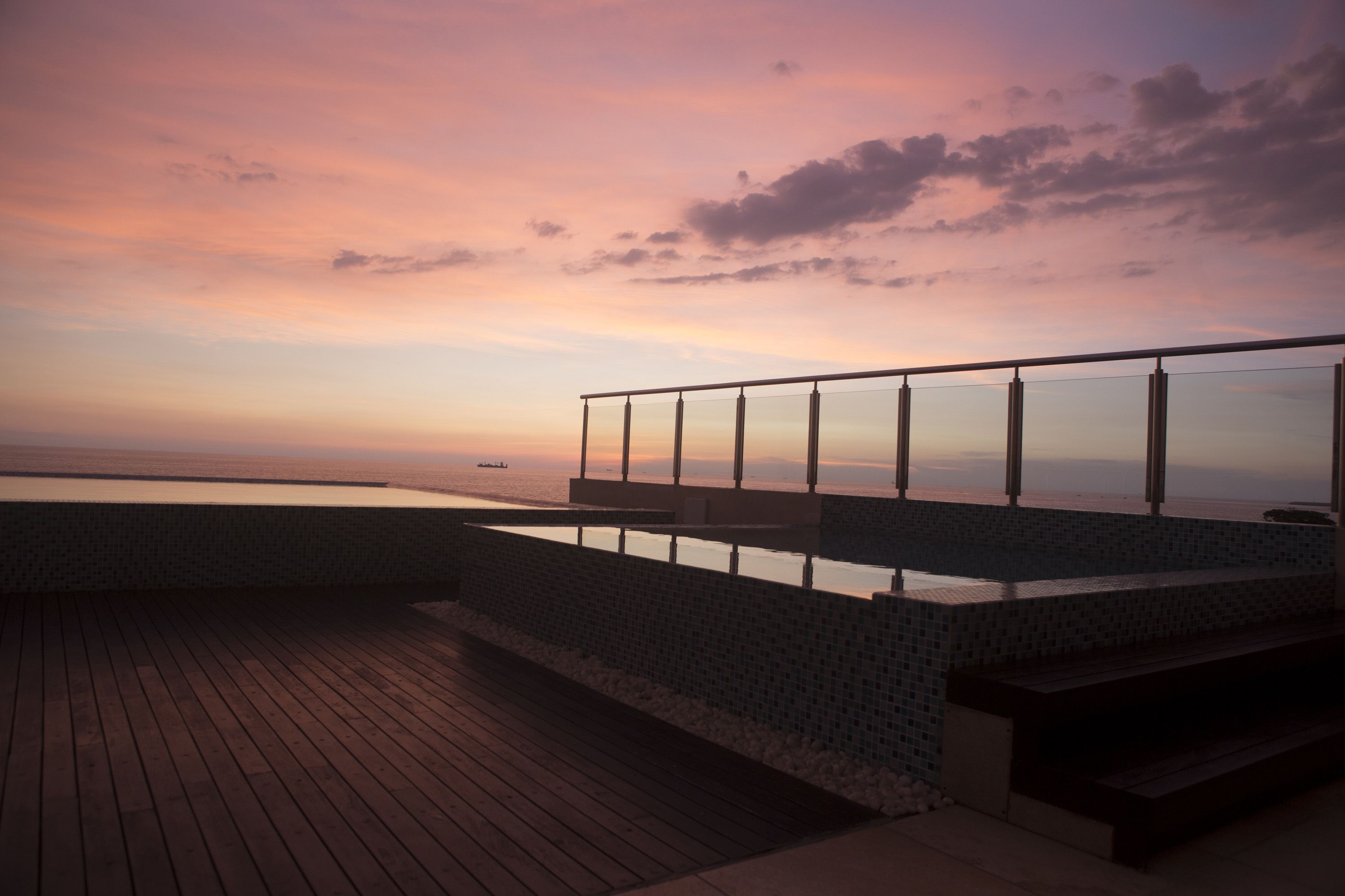 A wooden deck with a glass railing overlooking a body of water during sunset.