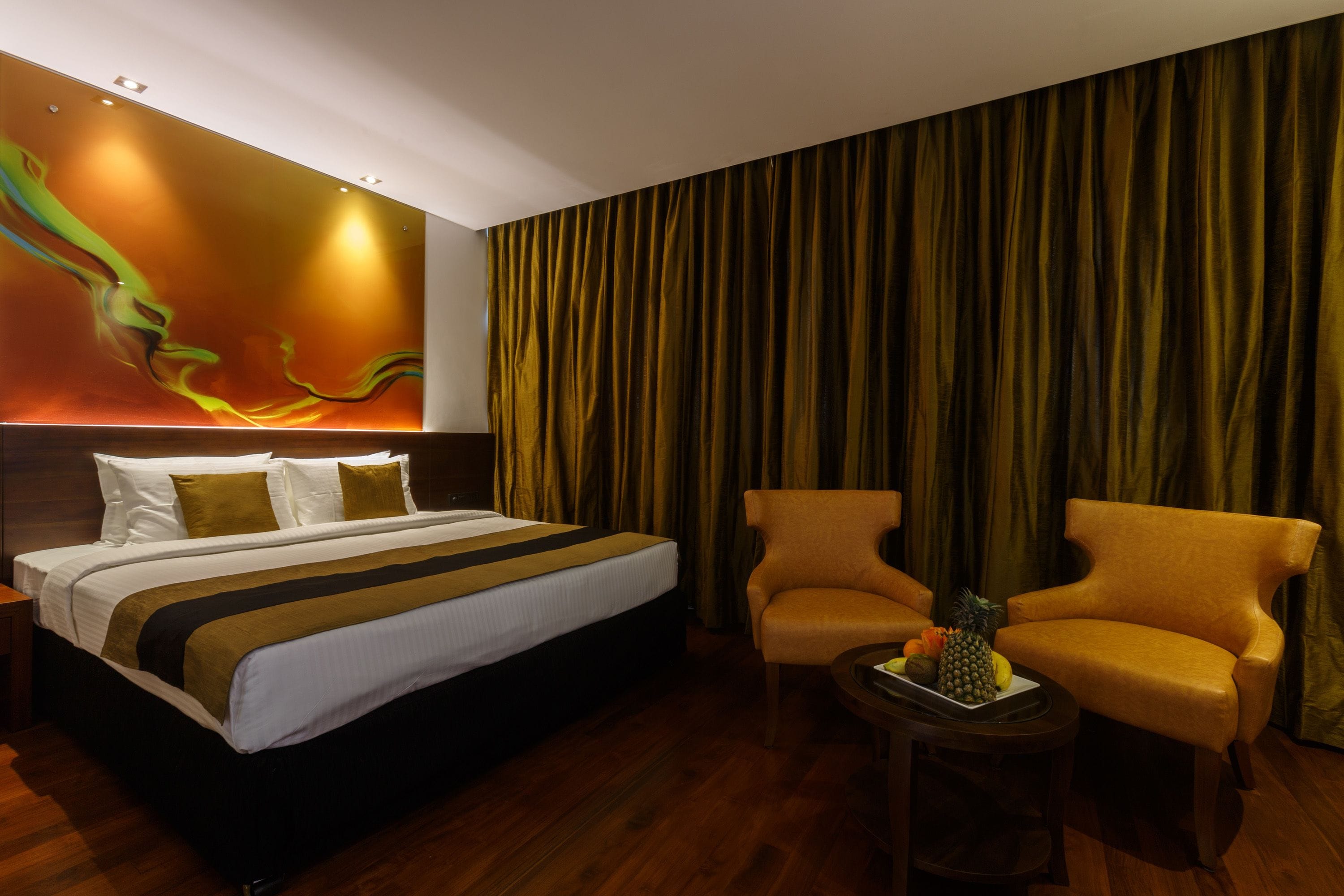 A hotel room with a large bed, two armchairs, a small table with fruit, and a wall mural.