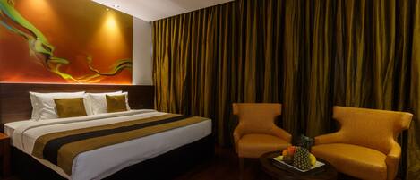A hotel room with a large bed, two armchairs, a small table with fruit, and a wall mural.