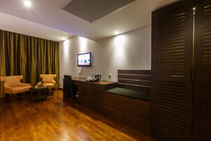 Una habitación de hotel moderna con suelo de madera, un escritorio con ordenador, televisor y sofá.