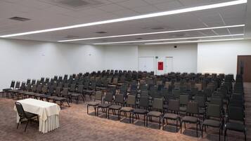 A large conference room with rows of chairs and a table, white walls, and a carpeted floor.