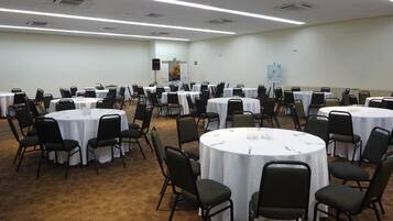 A conference room with multiple round tables, each surrounded by chairs, and white tablecloths.