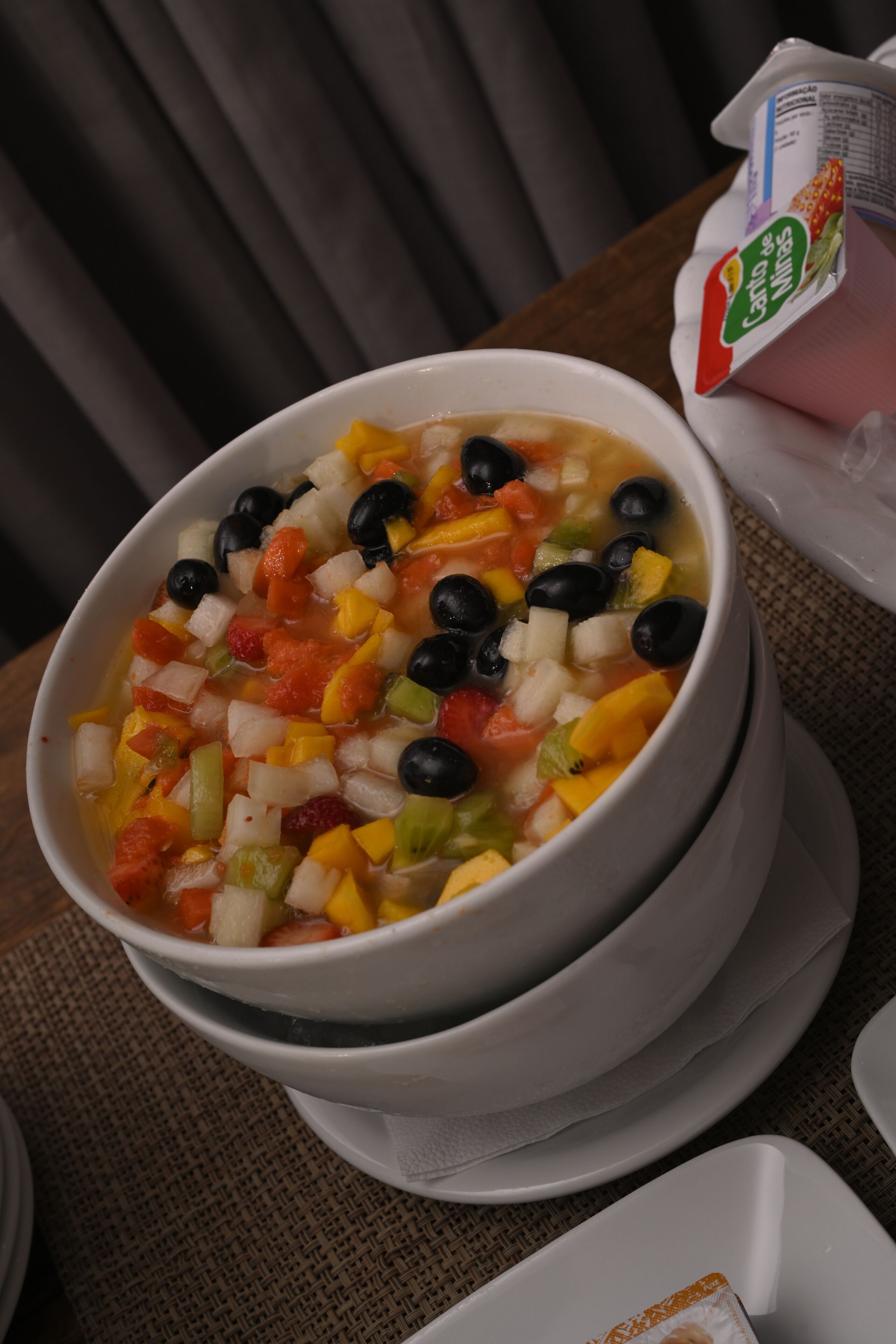 A bowl of vegetable soup with black olives, carrots, and celery on a table.