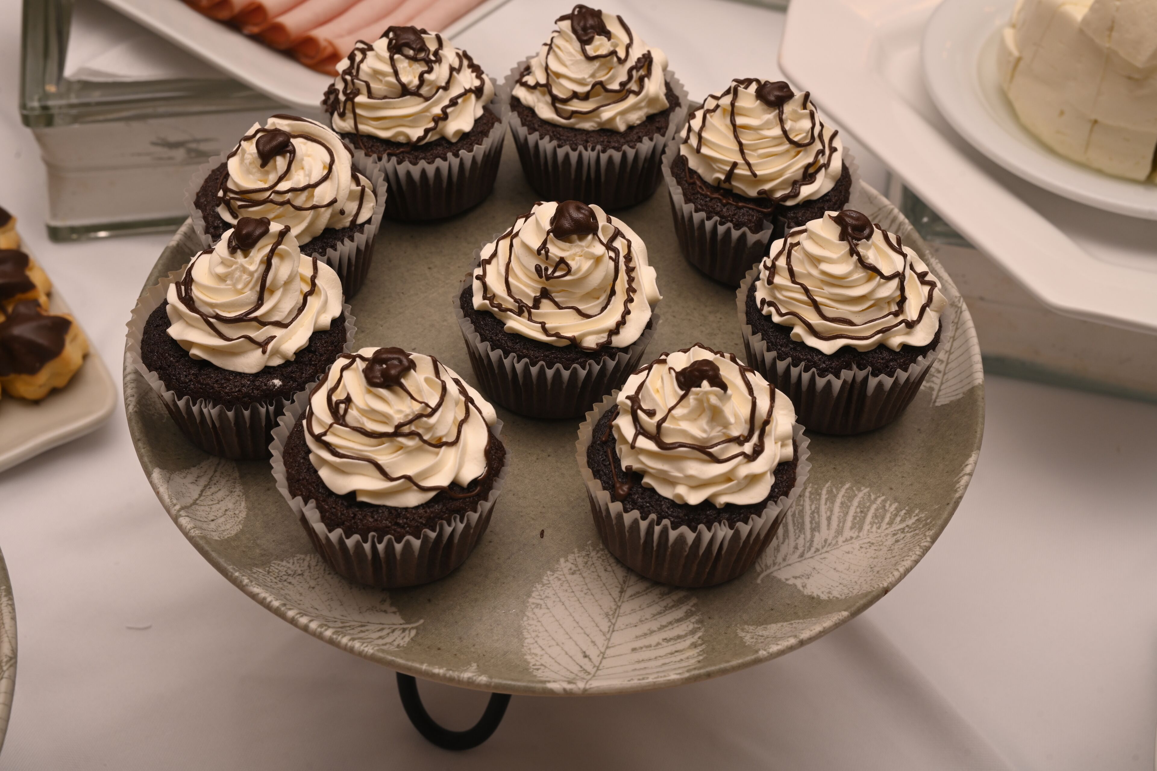 A tray of chocolate cupcakes with white frosting and chocolate drizzle.