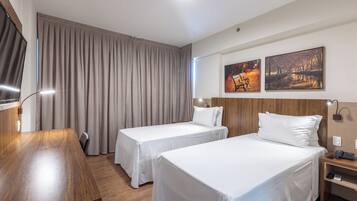 A hotel room with two single beds, a wooden desk, a TV, and two paintings on the wall.