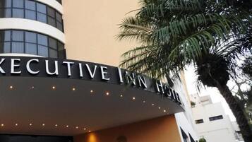 Exterior do Executive Inn Hotel, com uma placa visível e o logotipo do TripAdvisor indicando um prêmio Travelers' Choice de 2020.