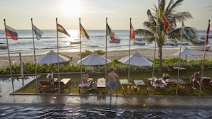 A poolside area with lounge chairs and umbrellas, overlooking a beach with flags and boats. - Coral Sands Hotel (Hikkaduwa)
