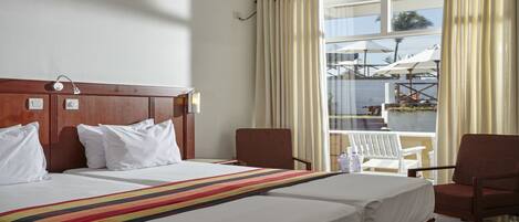 A hotel room with a large bed, two chairs, a small table, and a window with curtains.