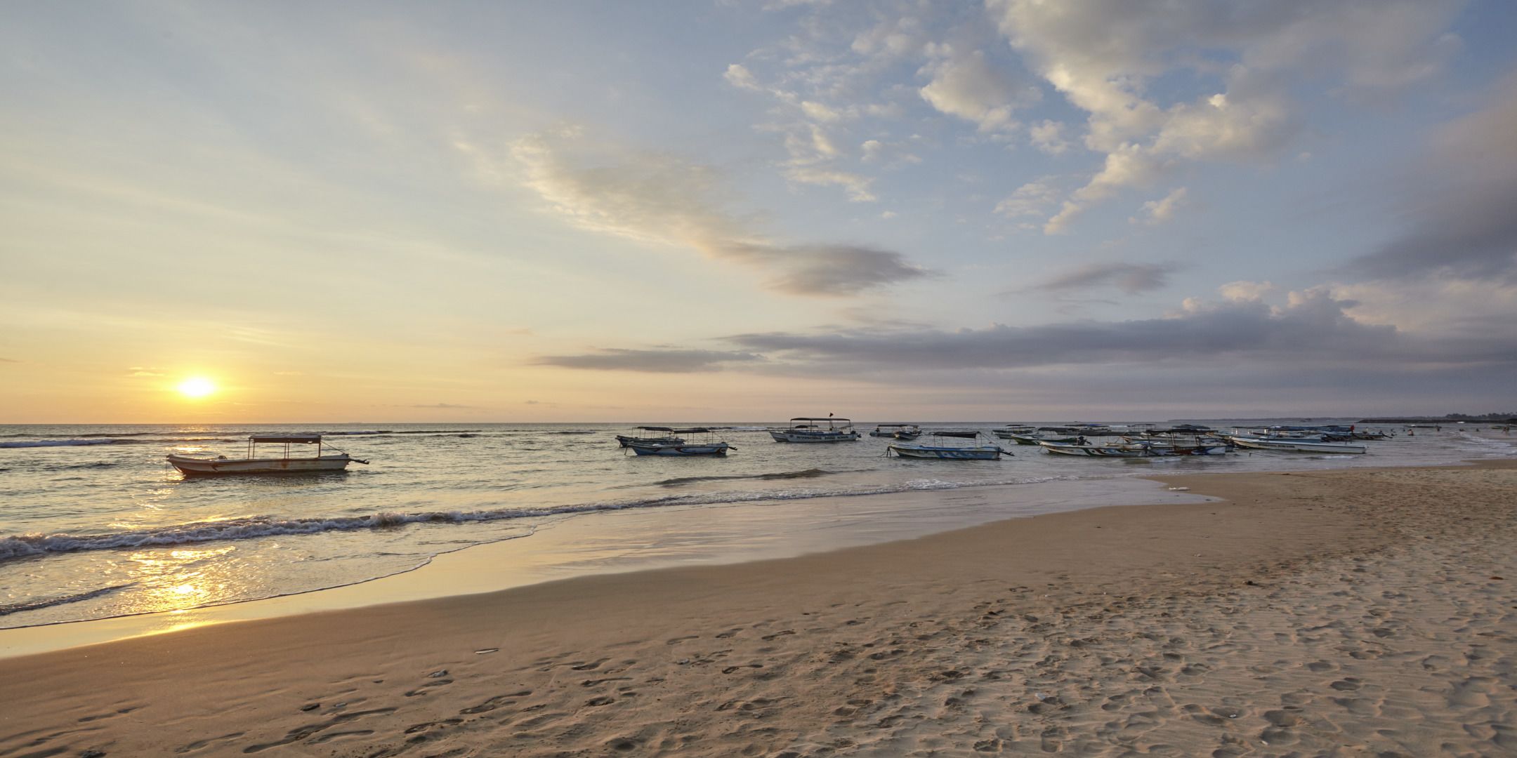 Une plage avec des bateaux et un coucher de soleil.
