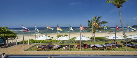 A poolside area with lounge chairs and umbrellas, flags, and a view of the beach and ocean.