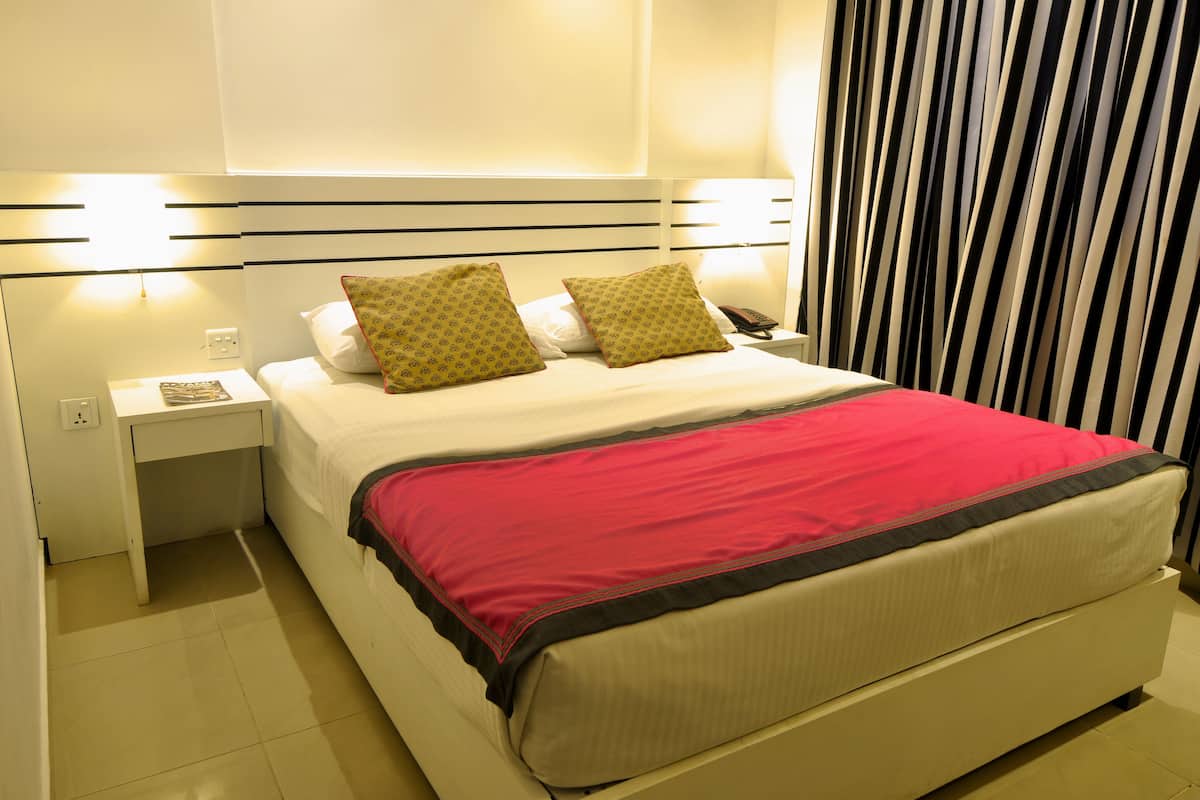 A neatly made bed with a red blanket, two pillows, and a bedside table with a lamp.