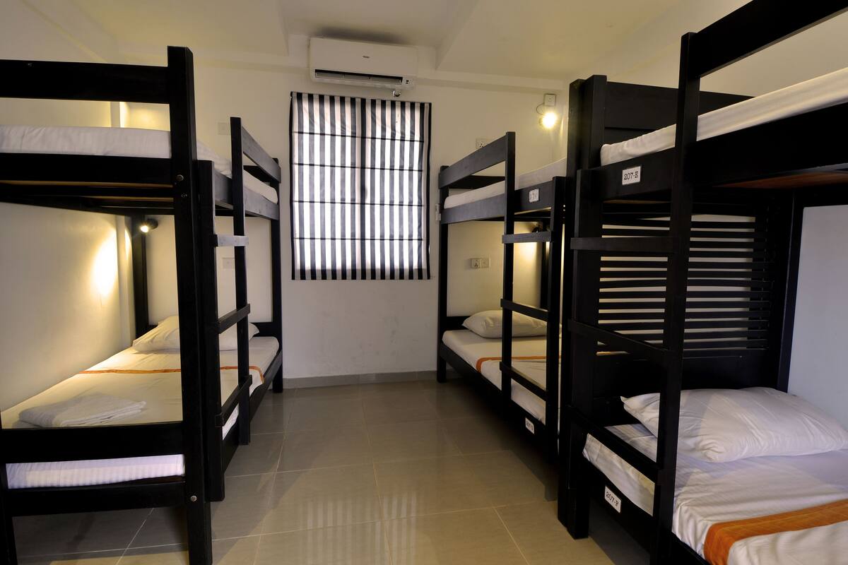 A room with four bunk beds, a window with vertical blinds, and an air conditioning unit on the wall.