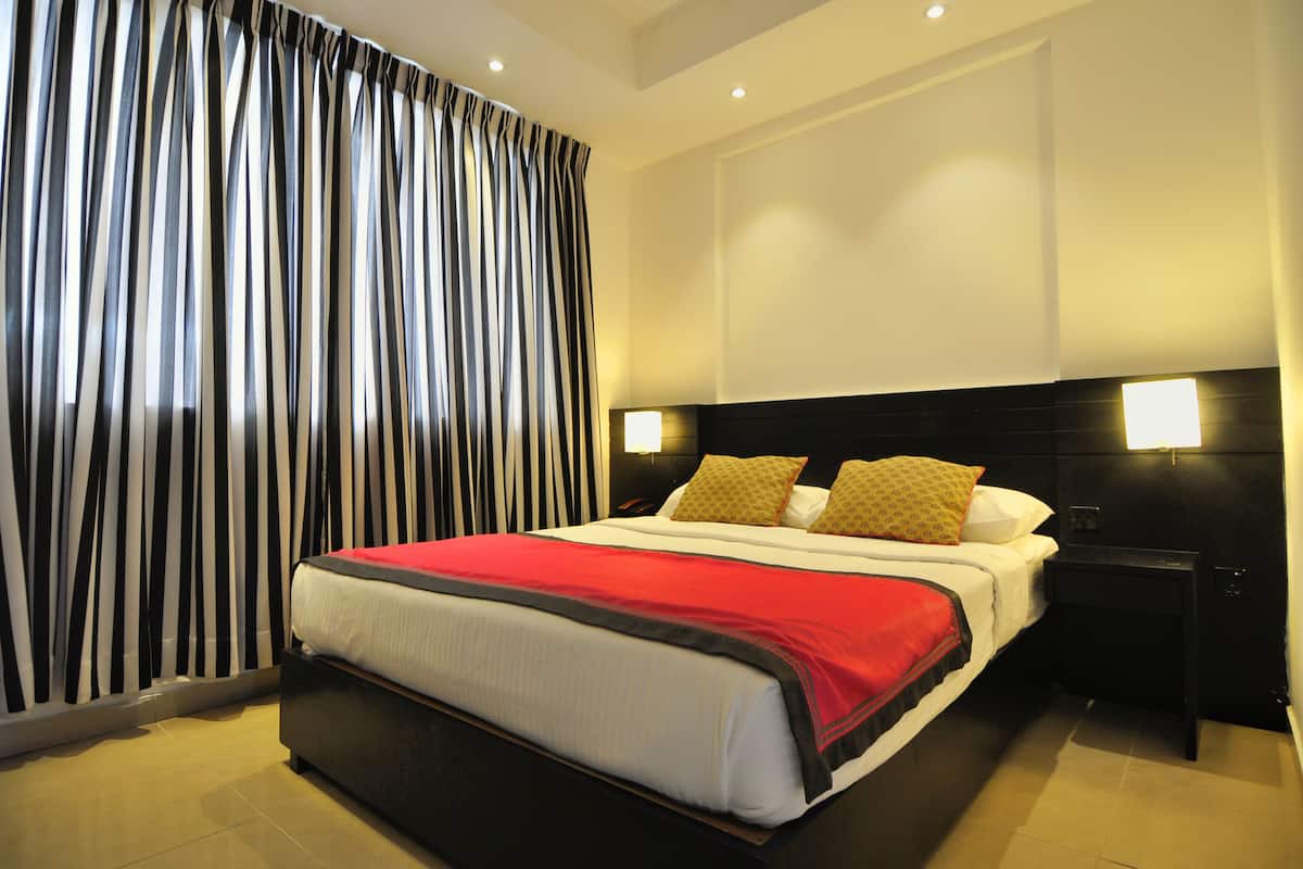 A hotel room with a large bed, black and white striped curtains, a red and black bedspread, and two bedside lamps.