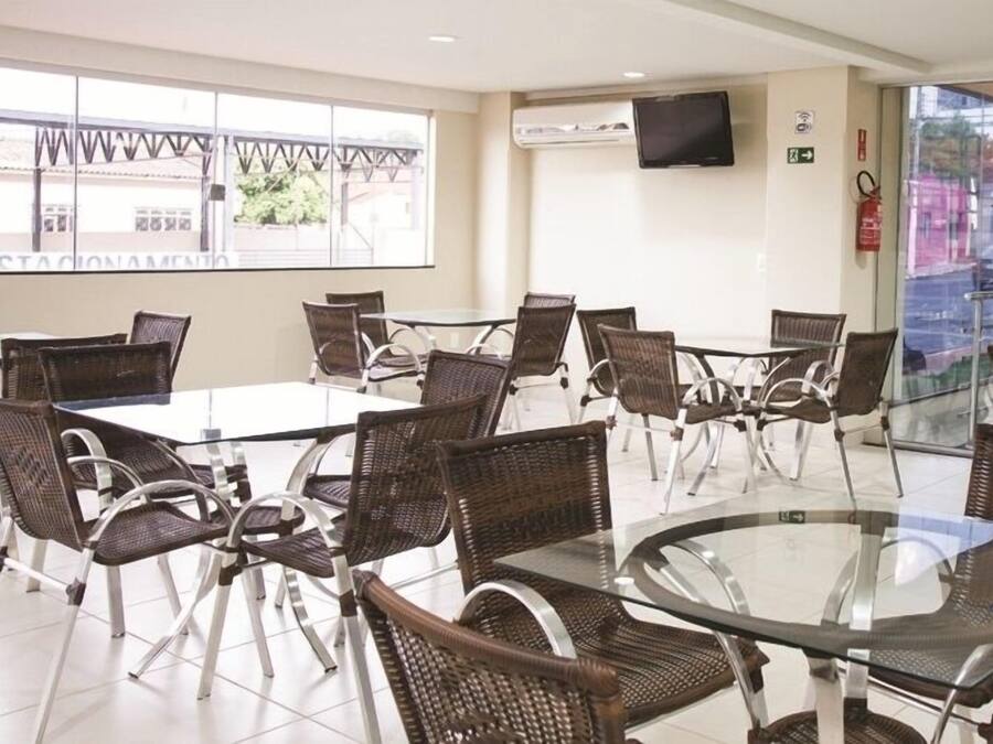 Un salón de conferencias con mesas de vidrio y sillas de mimbre, un televisor de pantalla plana en la pared y vistas al exterior a través de amplias ventanas.
