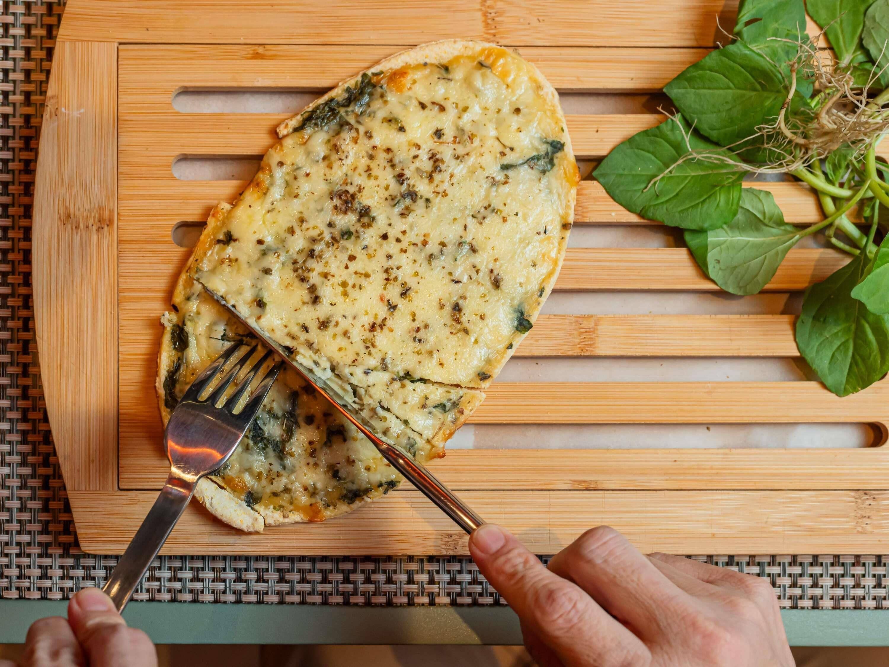 A person cutting a slice of pizza on a wooden cutting board.