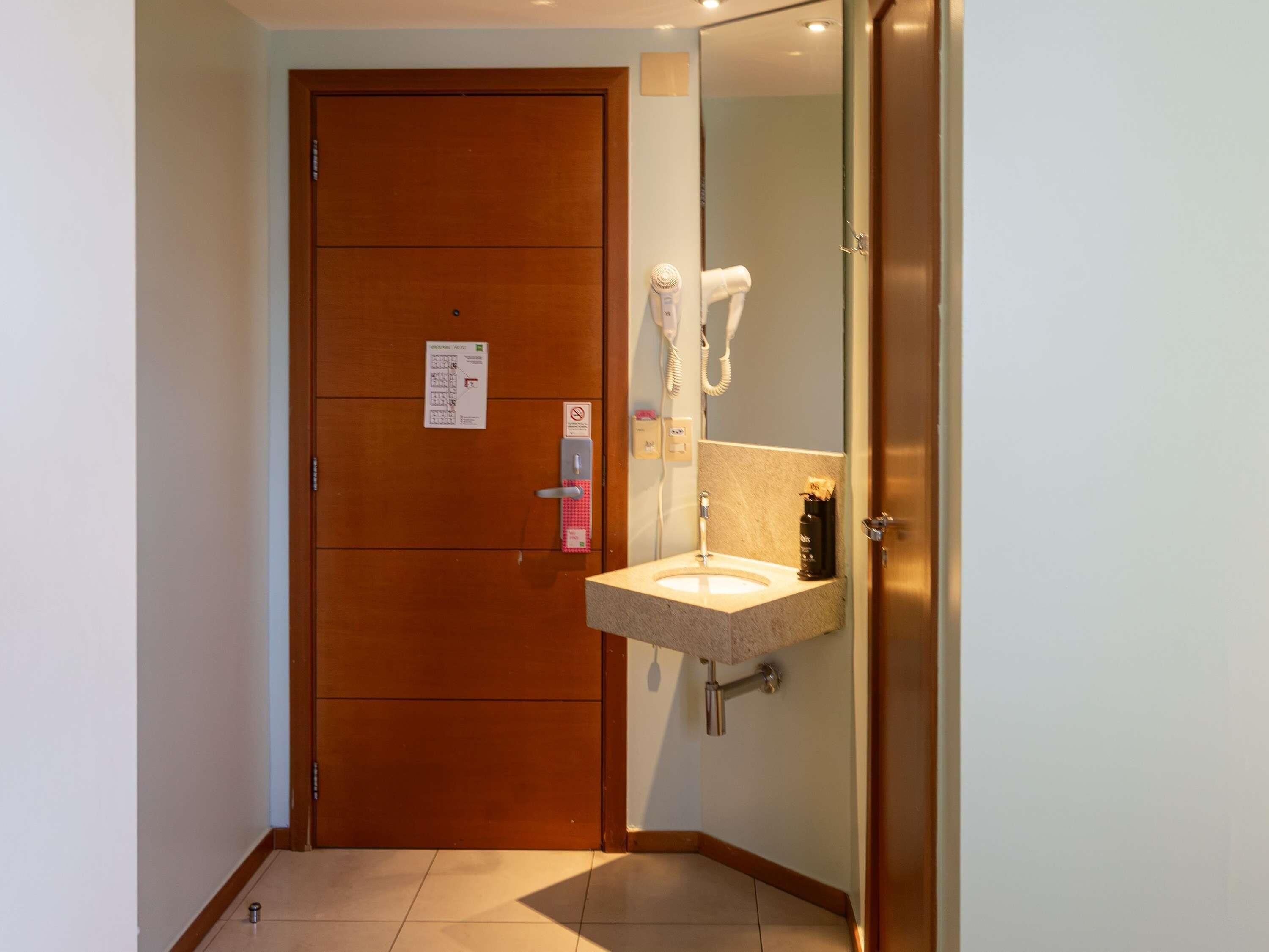 A hotel bathroom with a wooden door, a sink with a towel rack, and a mirror.