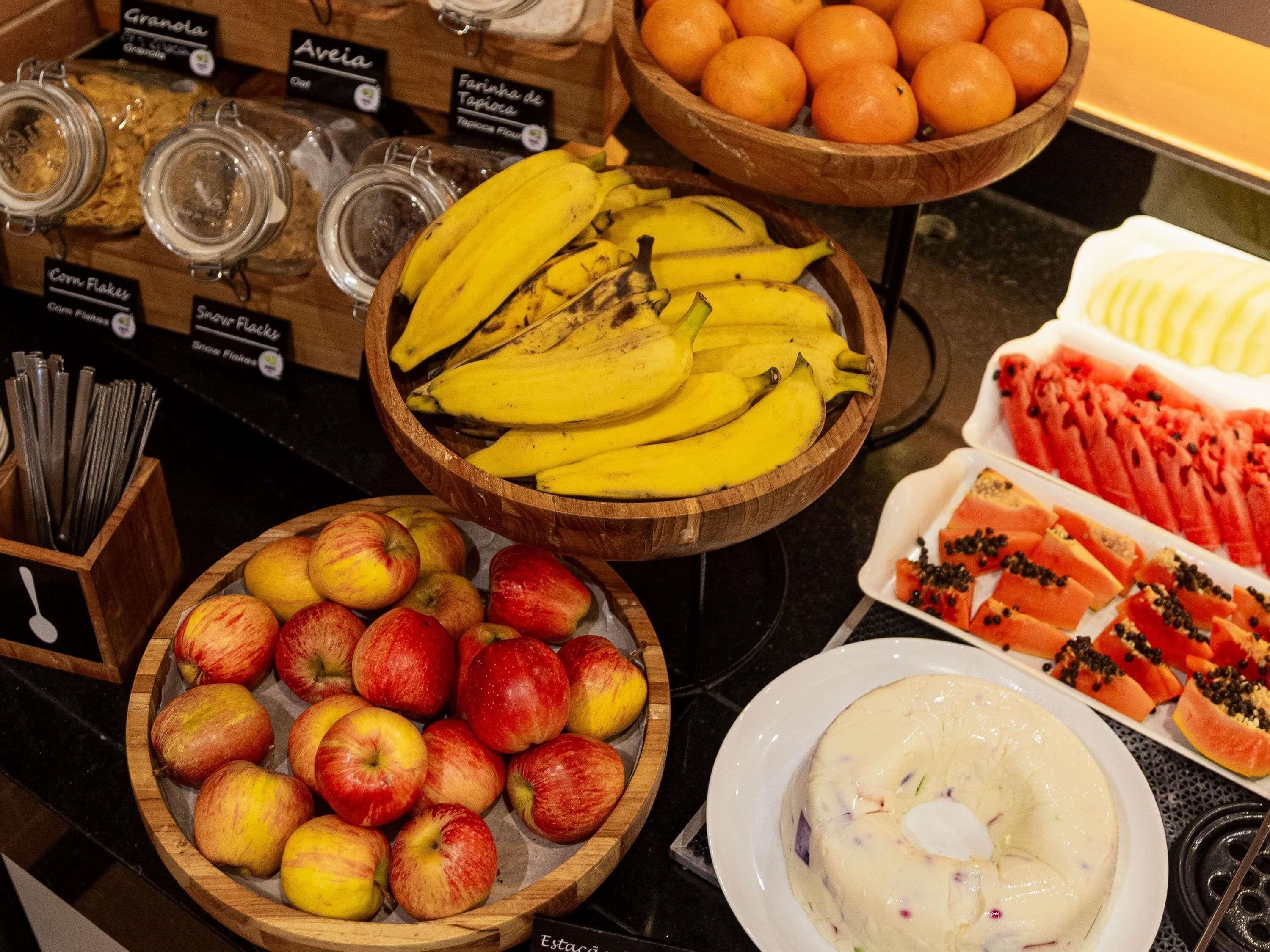Diversas frutas como bananas, maçãs, laranjas e mamão dispostas sobre um balcão.