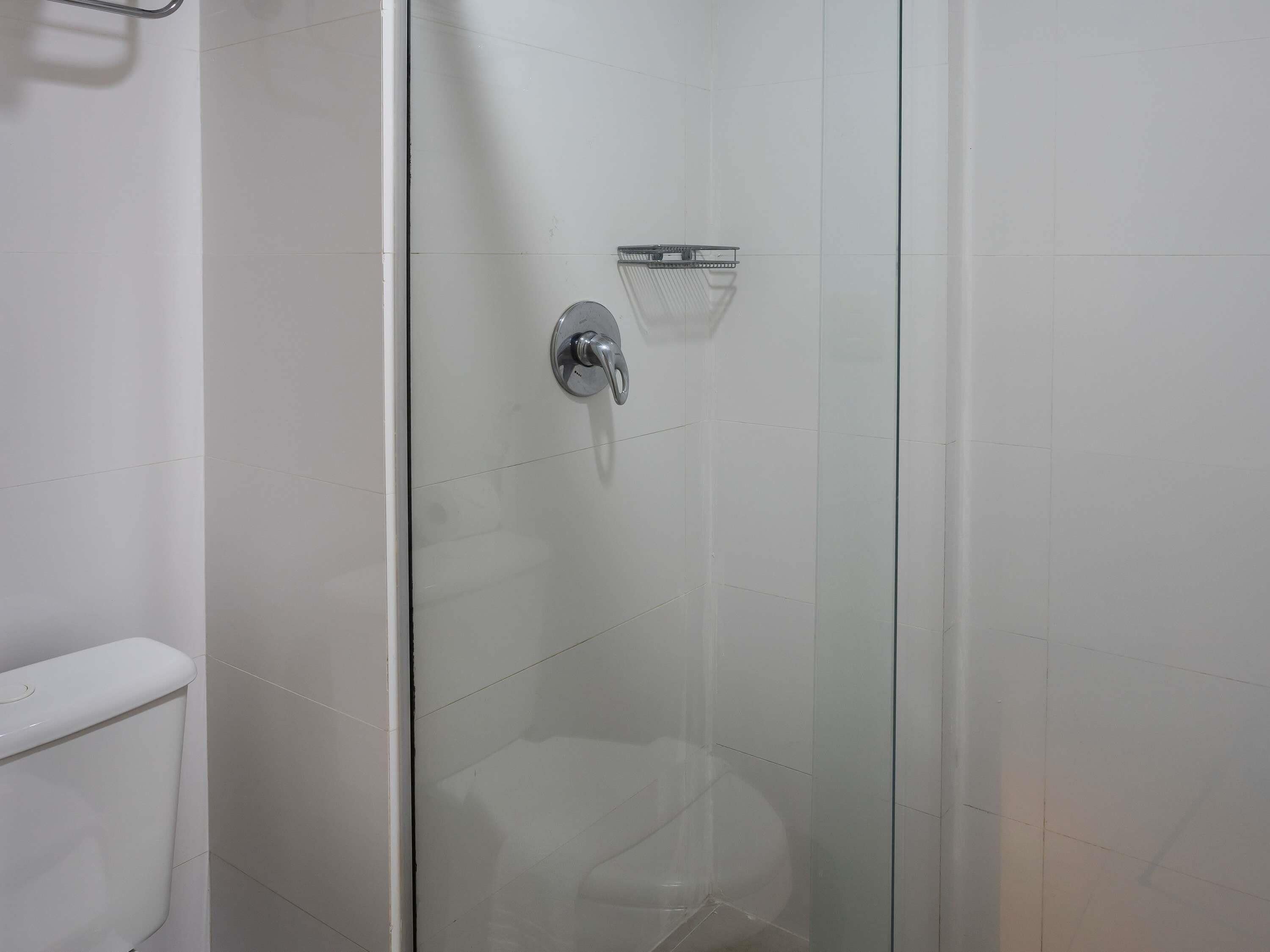 A glass-enclosed shower stall with a chrome showerhead and a small shelf.