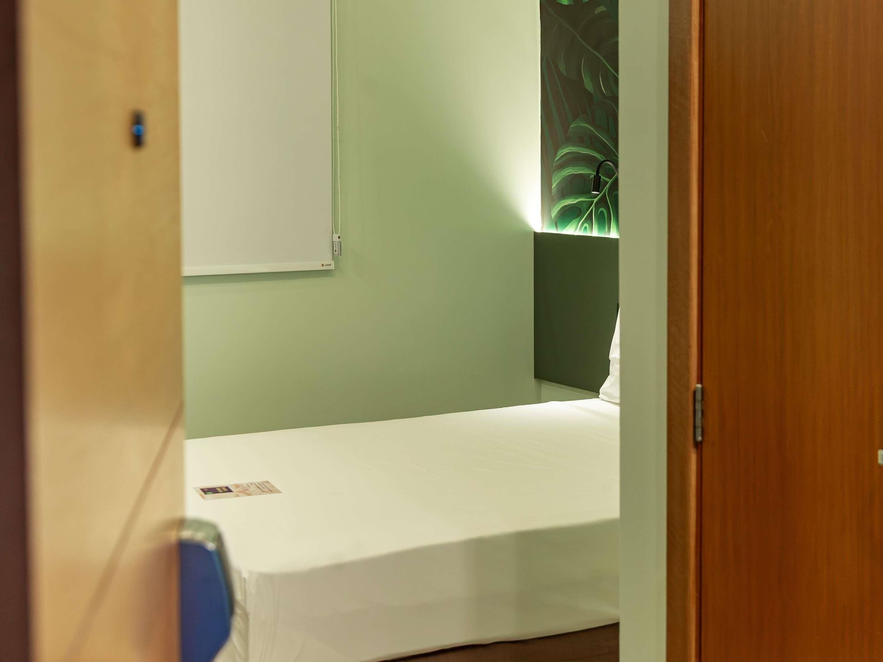 A single bed in a room with a green wall and a wooden door.